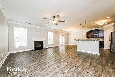 A spacious living room with a fireplace and a kitchen area in the background.