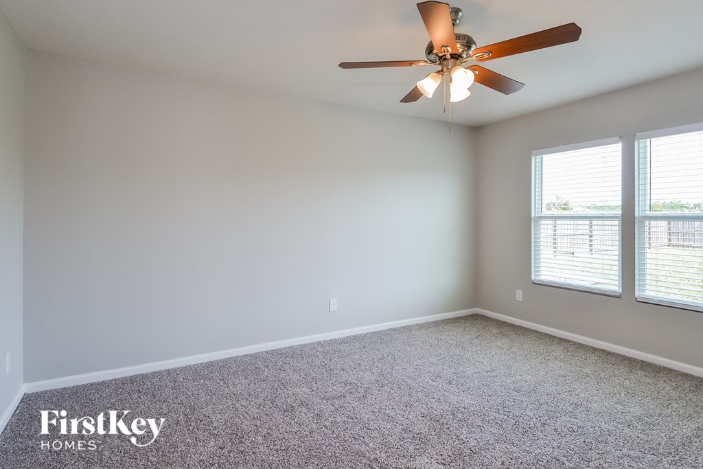an empty living room with a ceiling fan and two windows