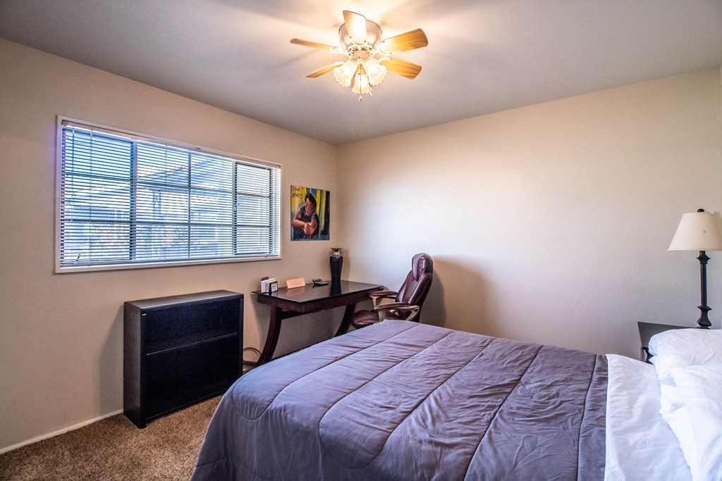 a bedroom with a bed and a desk and a ceiling fan