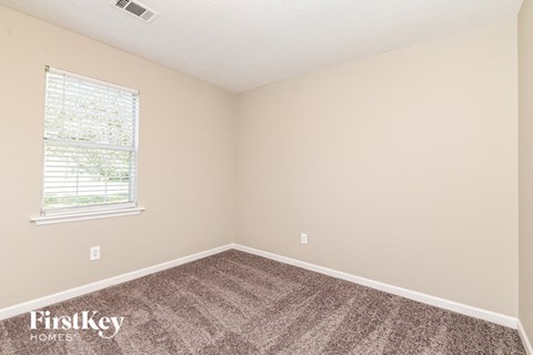 the bedroom of a small house with carpet and a window