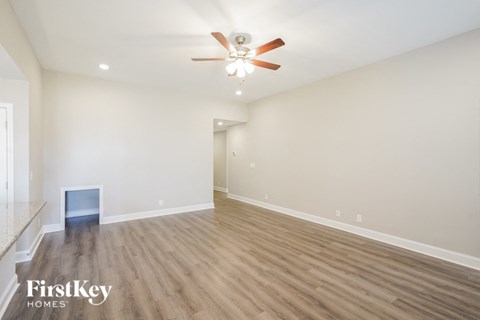 A spacious room with a ceiling fan and light fixture, and a wood floor.