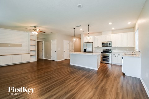an open kitchen and living room with white cabinets and wood flooring