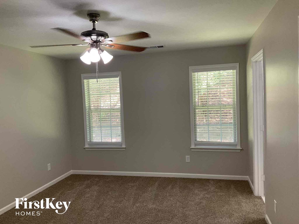 an empty bedroom with a ceiling fan and two windows