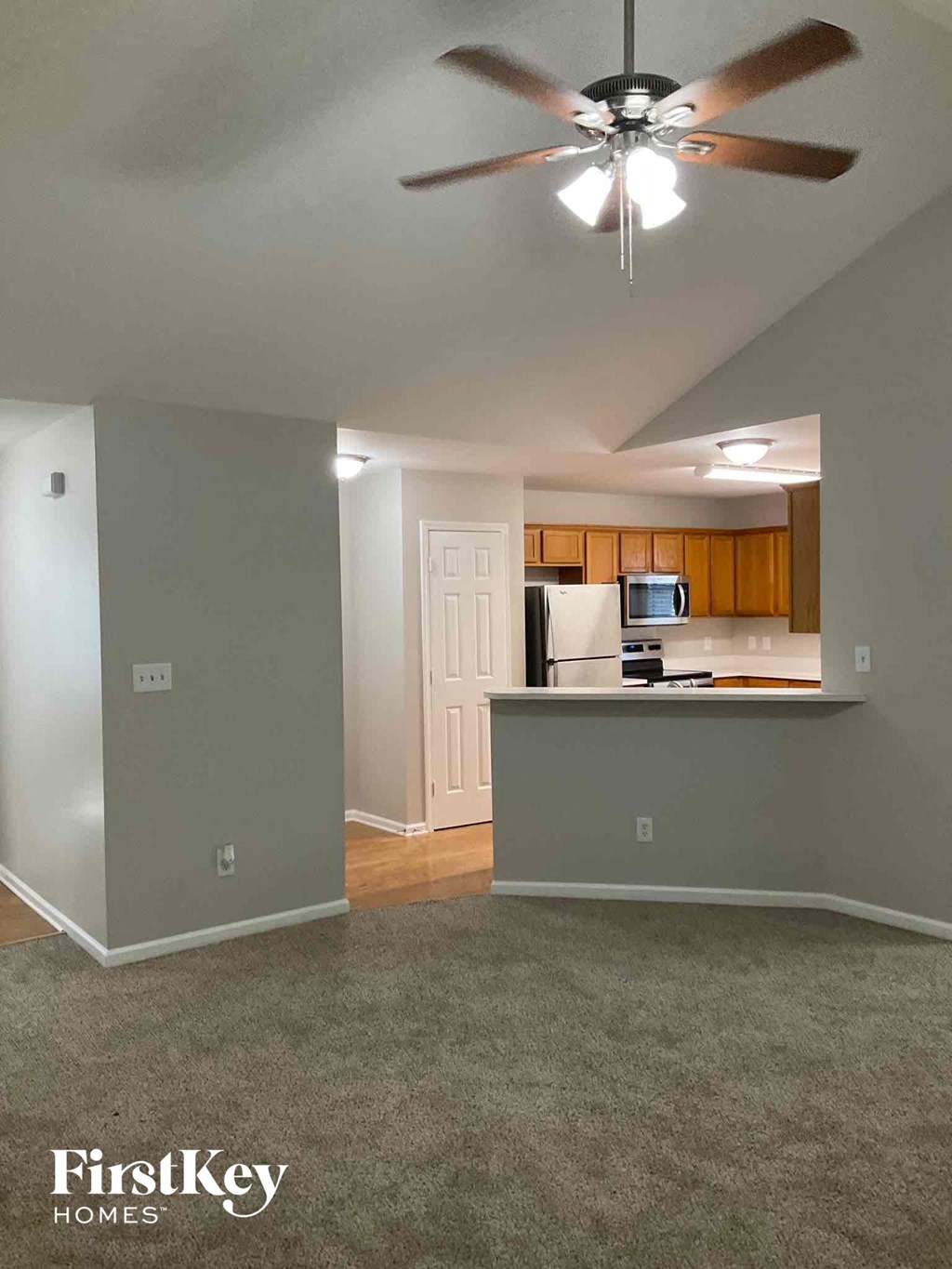 an empty living room and kitchen with a ceiling fan