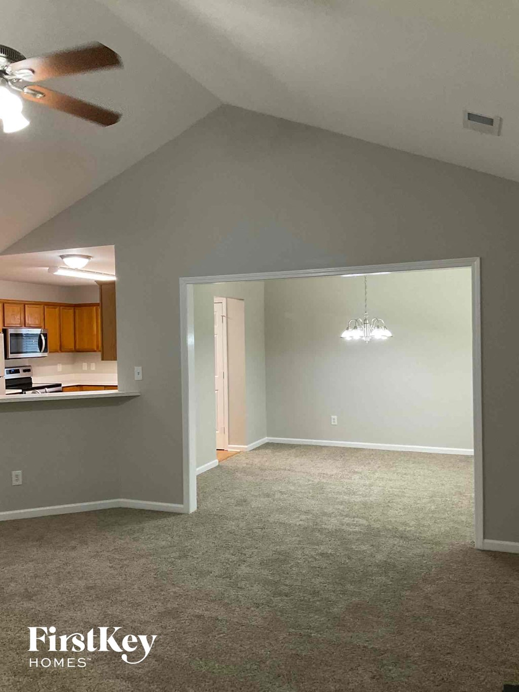 an empty living room with a ceiling fan and a kitchen