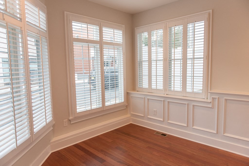 a bay window with white shutters in a room with a wooden floor