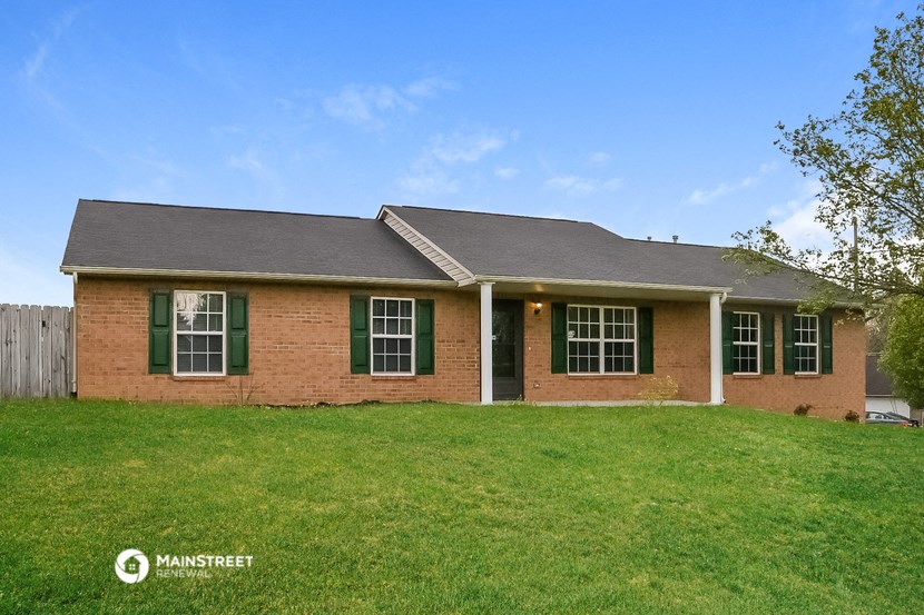 the front of a brick house with green shutters and a lawn