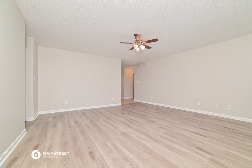the spacious living room with hardwood floors and a ceiling fan