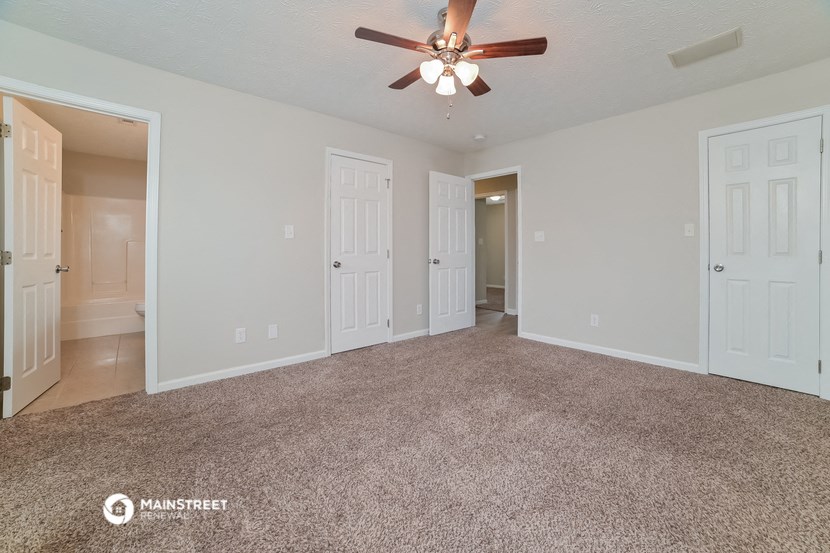 the living room of an apartment with carpet and a ceiling fan