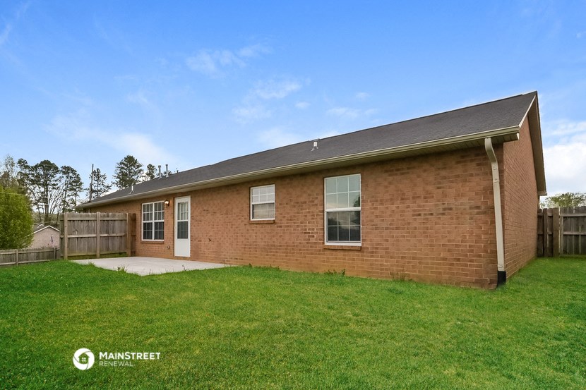 the front of a brick house with a green lawn and a wooden fence