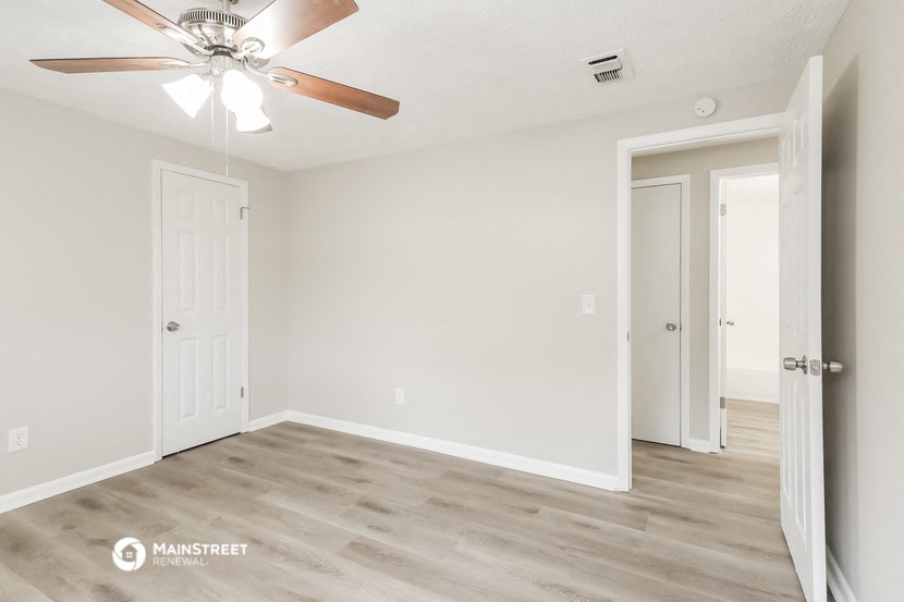 the spacious living room with a ceiling fan and a door to the bedroom