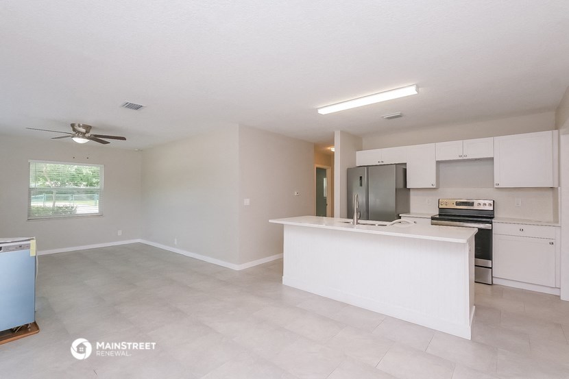 an empty kitchen and living room with white cabinets and a white counter top