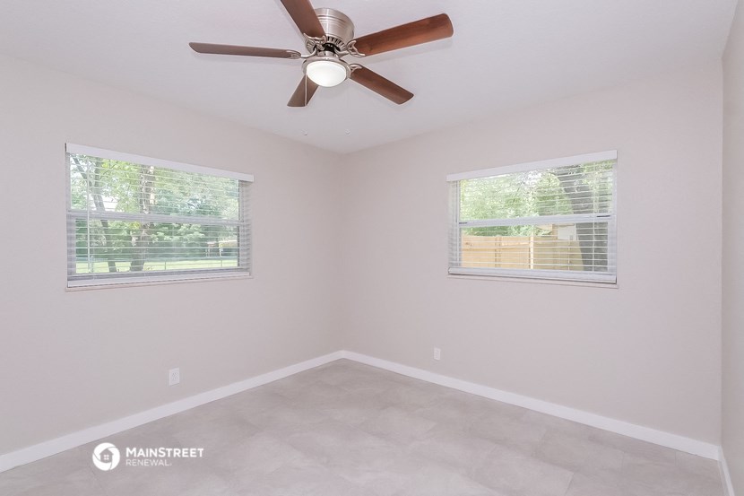 the spacious living room with two windows and a ceiling fan