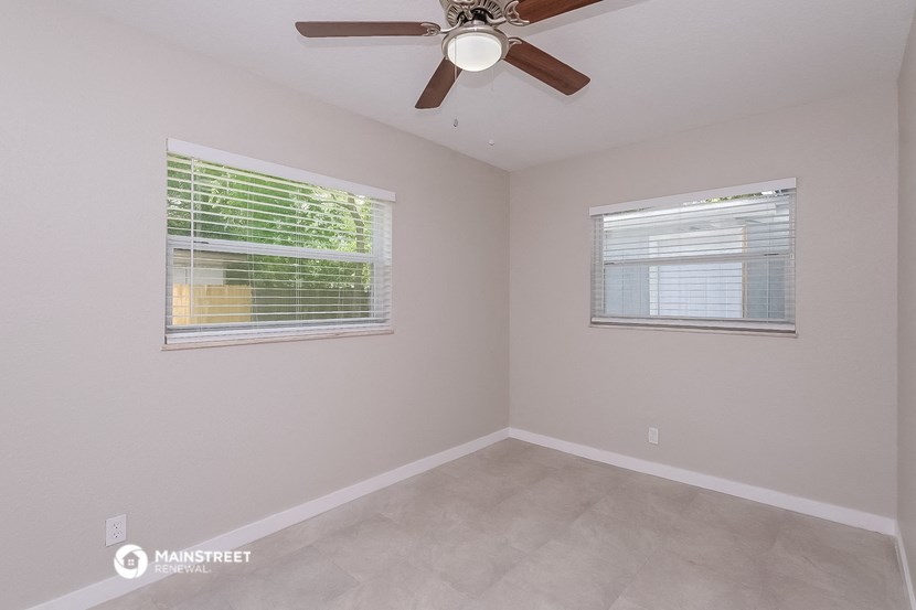 the spacious living room with two windows and a ceiling fan