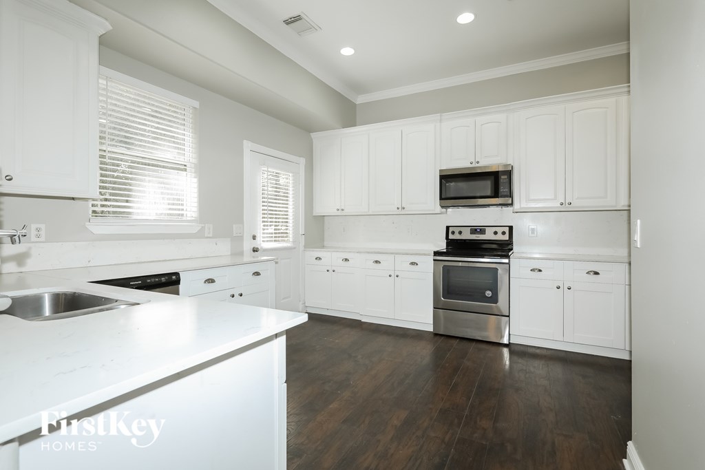 A modern kitchen with white cabinets and a wooden floor.