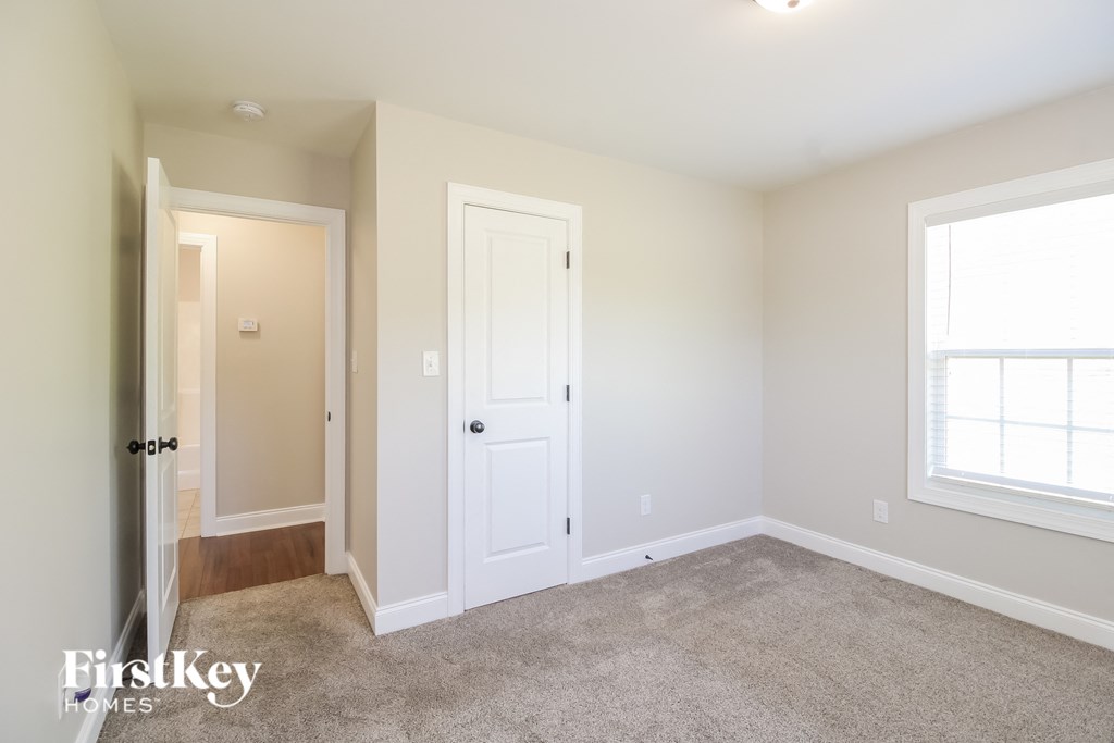 A room with a carpeted floor and a window with white blinds.