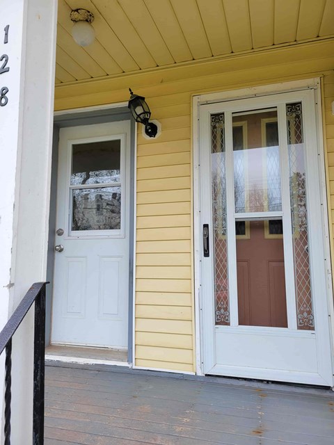 A white door with a glass window is on the right side of a yellow house.