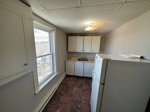 A kitchen with a refrigerator, cabinets, and a window.