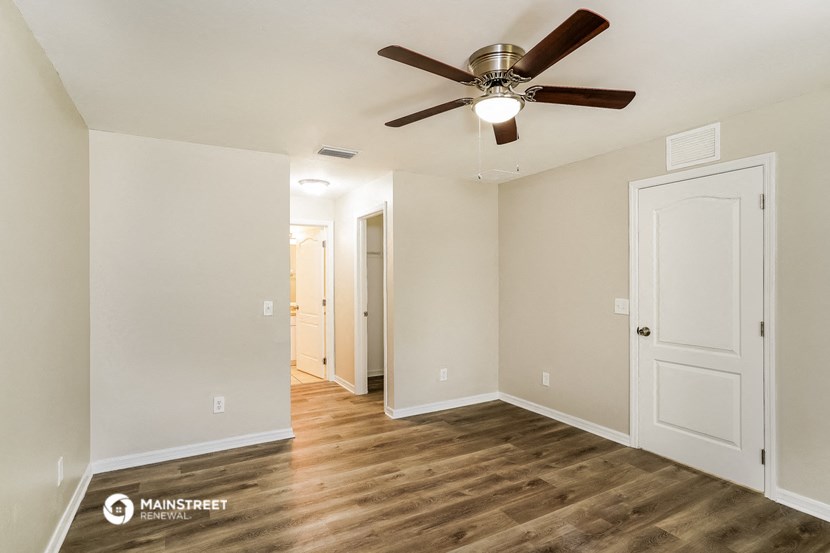 the living room and dining room of an apartment with wood floors and a ceiling fan