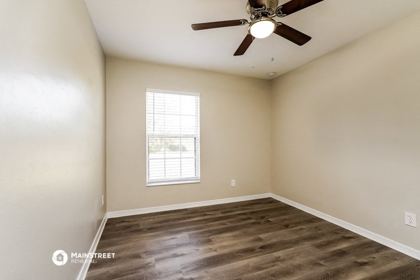the spacious living room with wood flooring and a ceiling fan