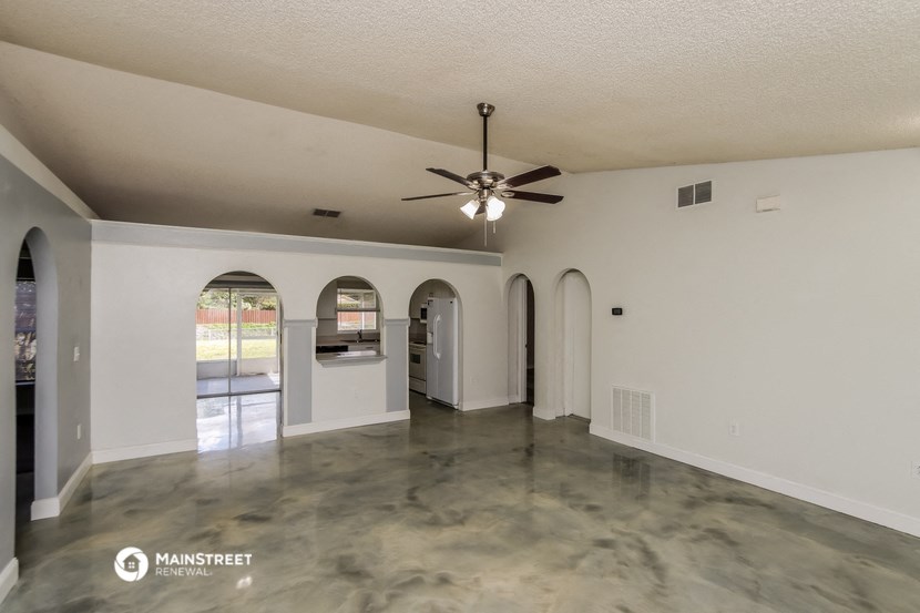 an empty living room with a ceiling fan and a kitchen