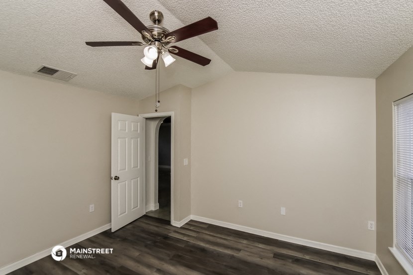 the spacious living room with ceiling fan and door to the hallway
