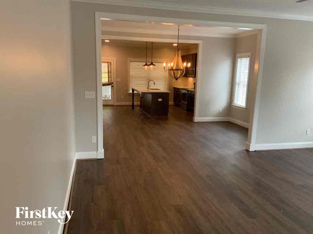 A spacious living room with wood flooring and a kitchen in the background.
