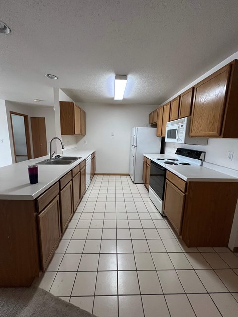 A kitchen with white tile floors and wooden cabinets.