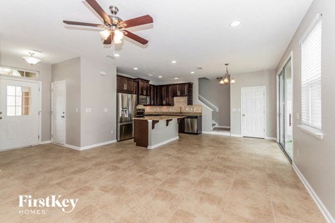 an empty living room with a kitchen and a ceiling fan