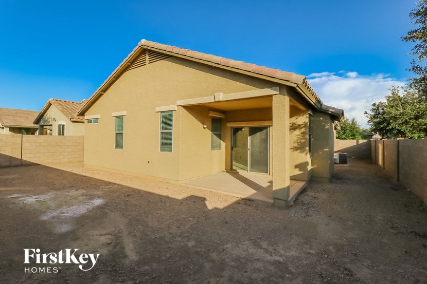the backyard of a yellow house with a driveway and a fence