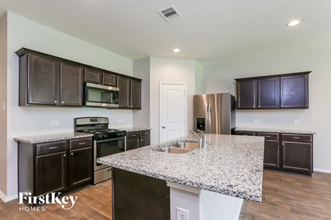 A kitchen with granite countertops and dark brown cabinets.