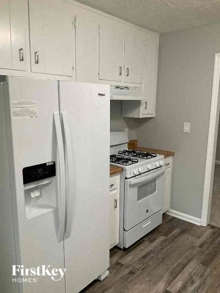 A white refrigerator with a black water filter drawer is in a kitchen with white cabinets.
