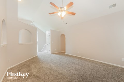 a spacious living room with carpet and a ceiling fan