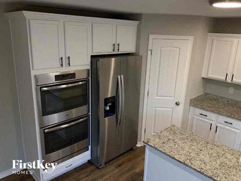 A kitchen with a stainless steel refrigerator and oven, and white cabinets.