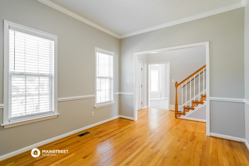 the living room and entryway of a house with wood floors and a staircase