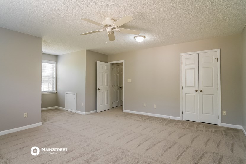 the spacious living room with white carpet and a ceiling fan