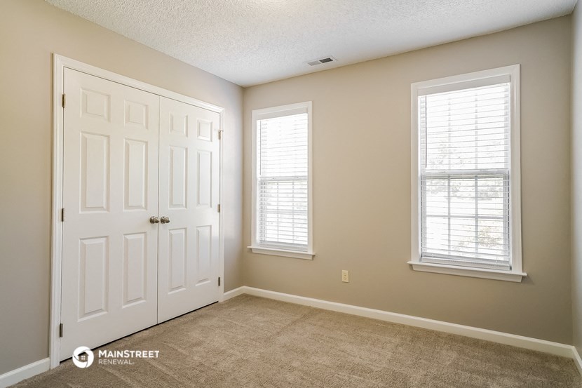 the living room of a home with a white door and two windows