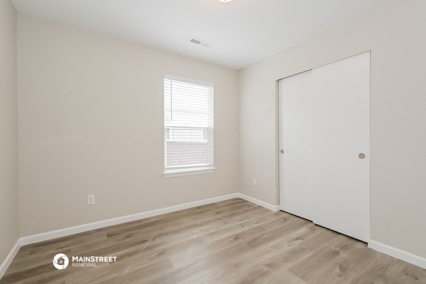 a bedroom with white walls and wood flooring and a closet