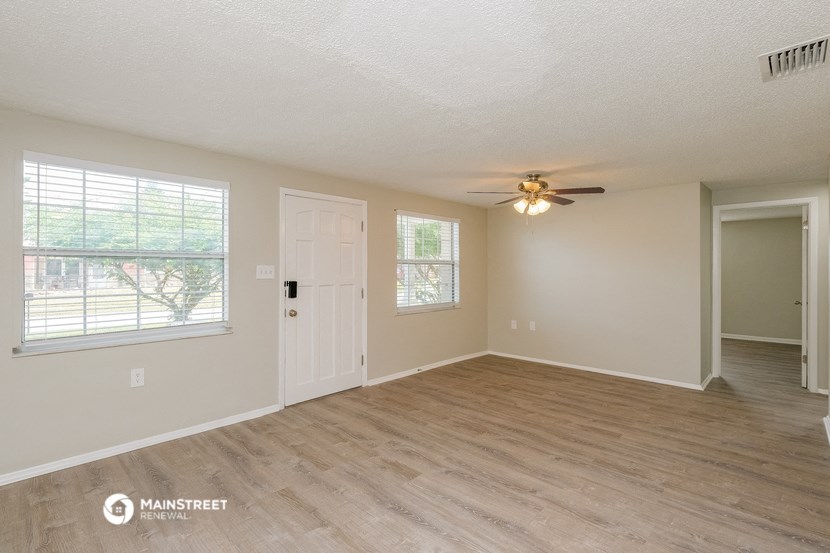 the spacious living room with hardwood flooring and a ceiling fan