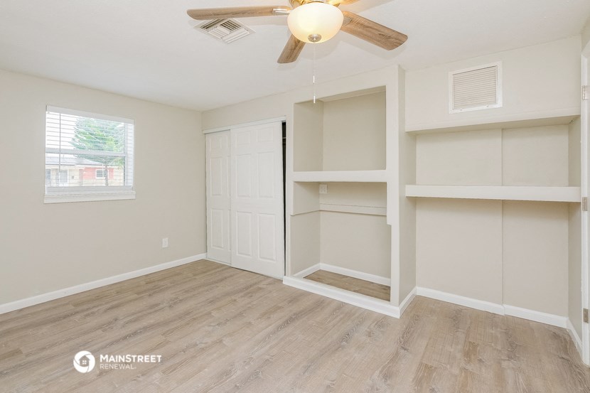 the spacious living room with built in shelves and a ceiling fan