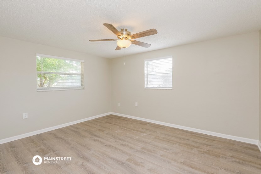 the spacious living room with wood flooring and a ceiling fan