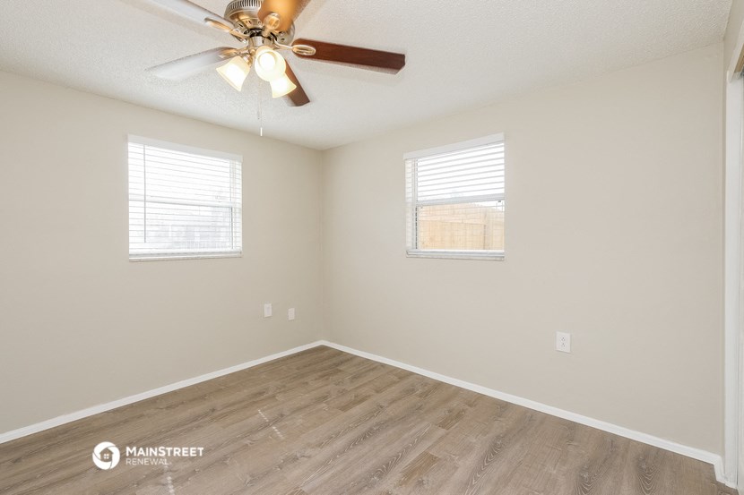 the spacious living room with wood flooring and a ceiling fan