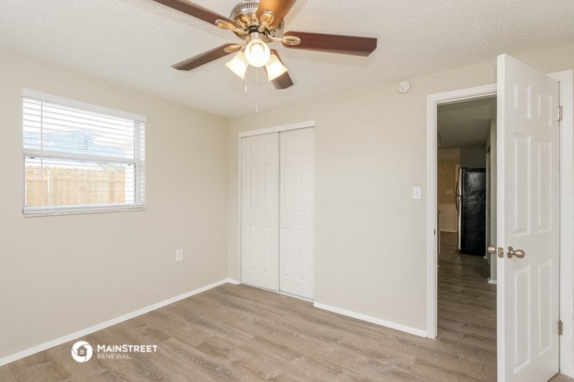 the spacious living room with a ceiling fan and a door to the bedroom