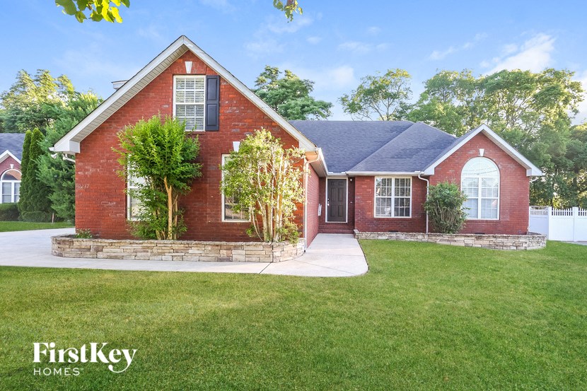 a red brick house with a green lawn and a white fence