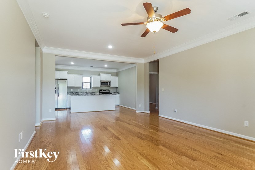 an empty living room with a ceiling fan and a kitchen
