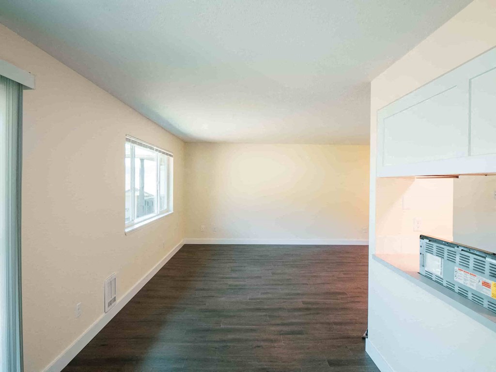 an empty living room and kitchen with hardwood flooring and a window