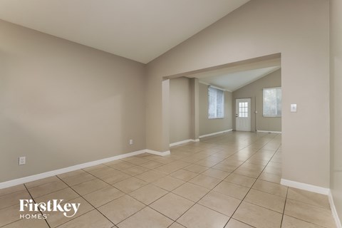a large empty living room with tiled flooring and a door into a hallway