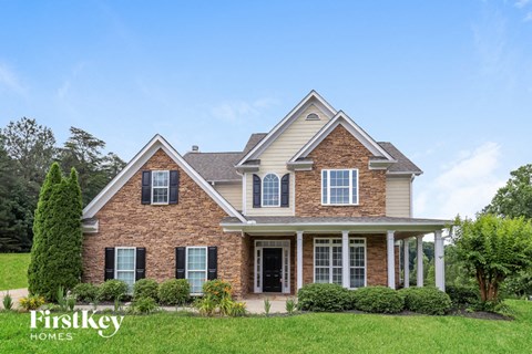 A brick house with a porch and a tree in front.
