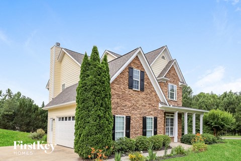 A brick house with a large front yard and a tall tree.