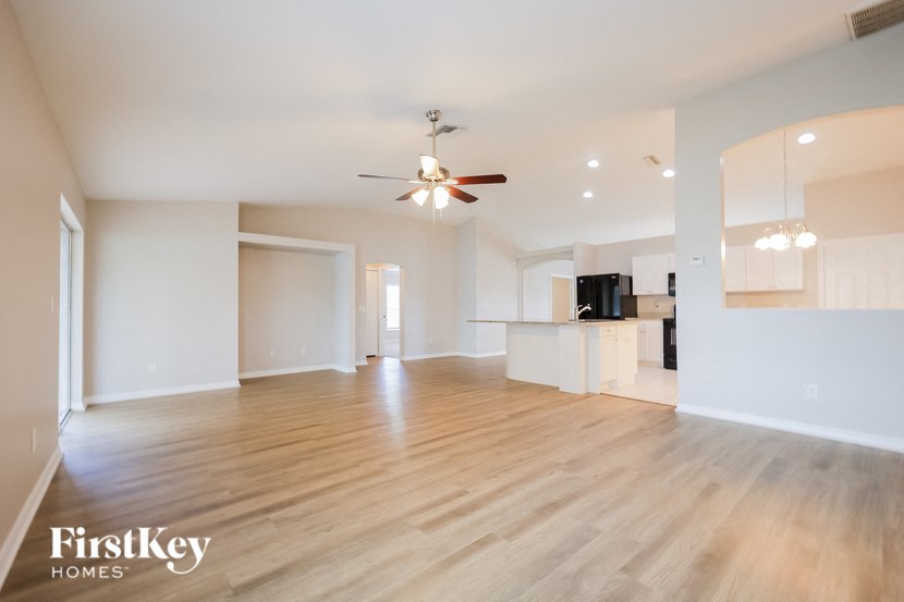 an empty living room with a ceiling fan and a kitchen